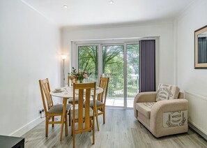 A dining area with a round table, wooden chairs, and a vase of flowers. There is a sofa with a cushion and a radiator.