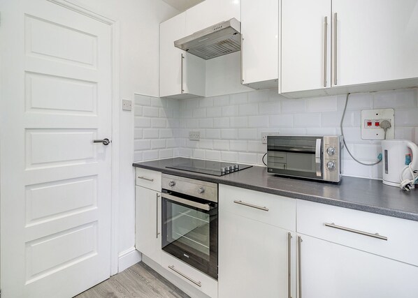 Una cocina con gabinetes blancos, horno empotrado, tostadora y microondas.