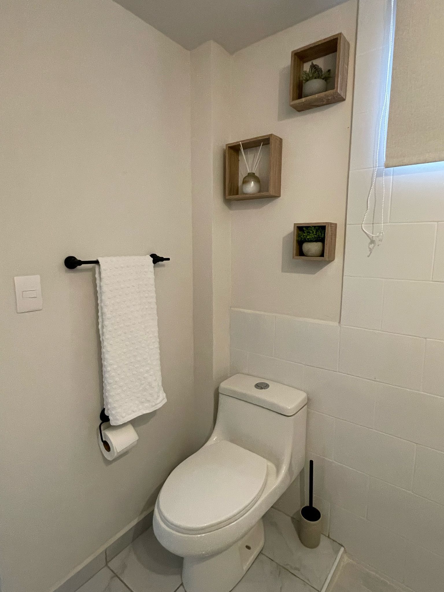 Ein Badezimmer mit Toilette, einem Handtuchhalter und zwei kleinen Holzregalen mit Pflanzen.