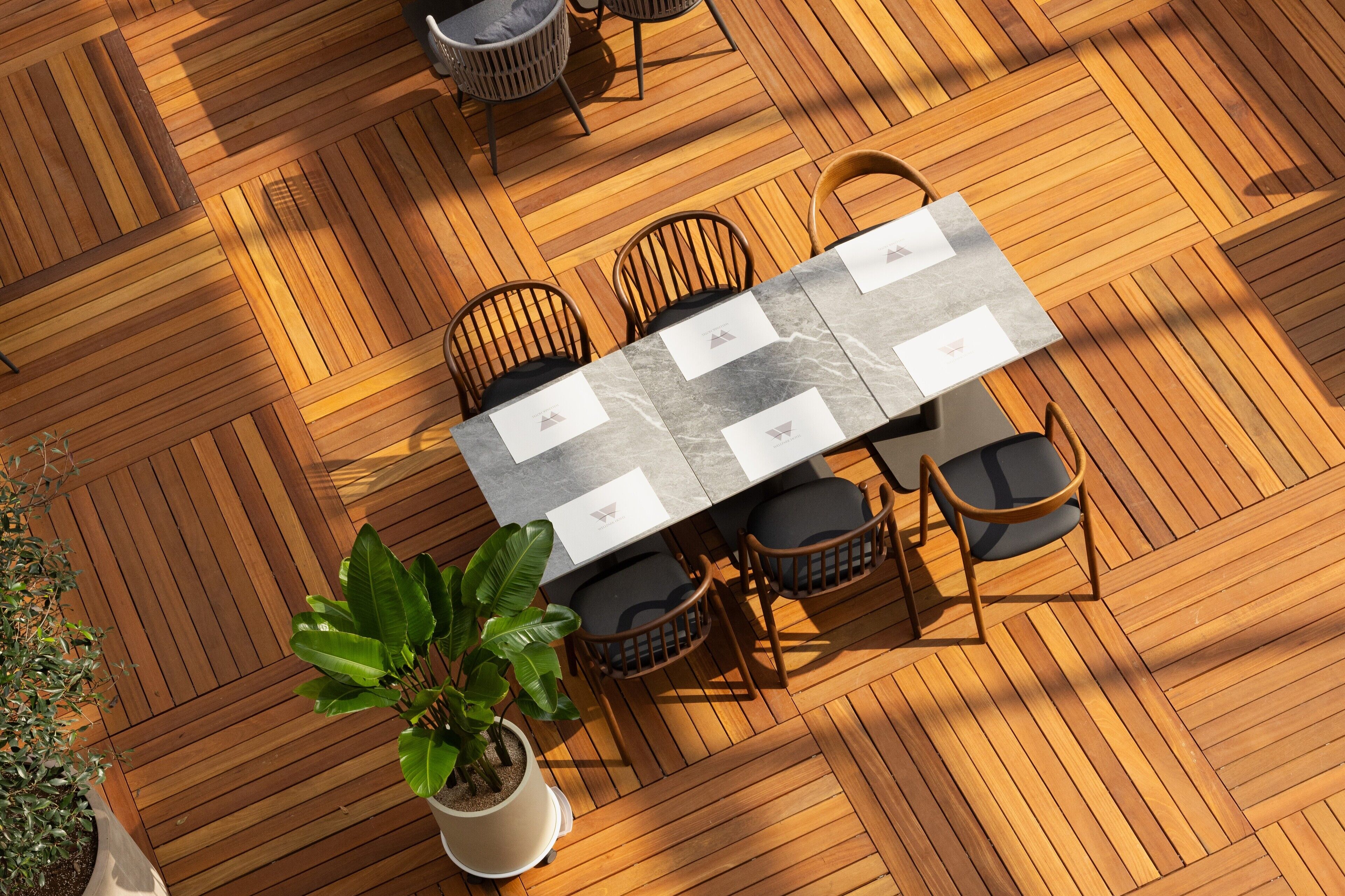 Una terraza de madera con una mesa rectangular y seis sillas, rodeada de plantas en macetas.