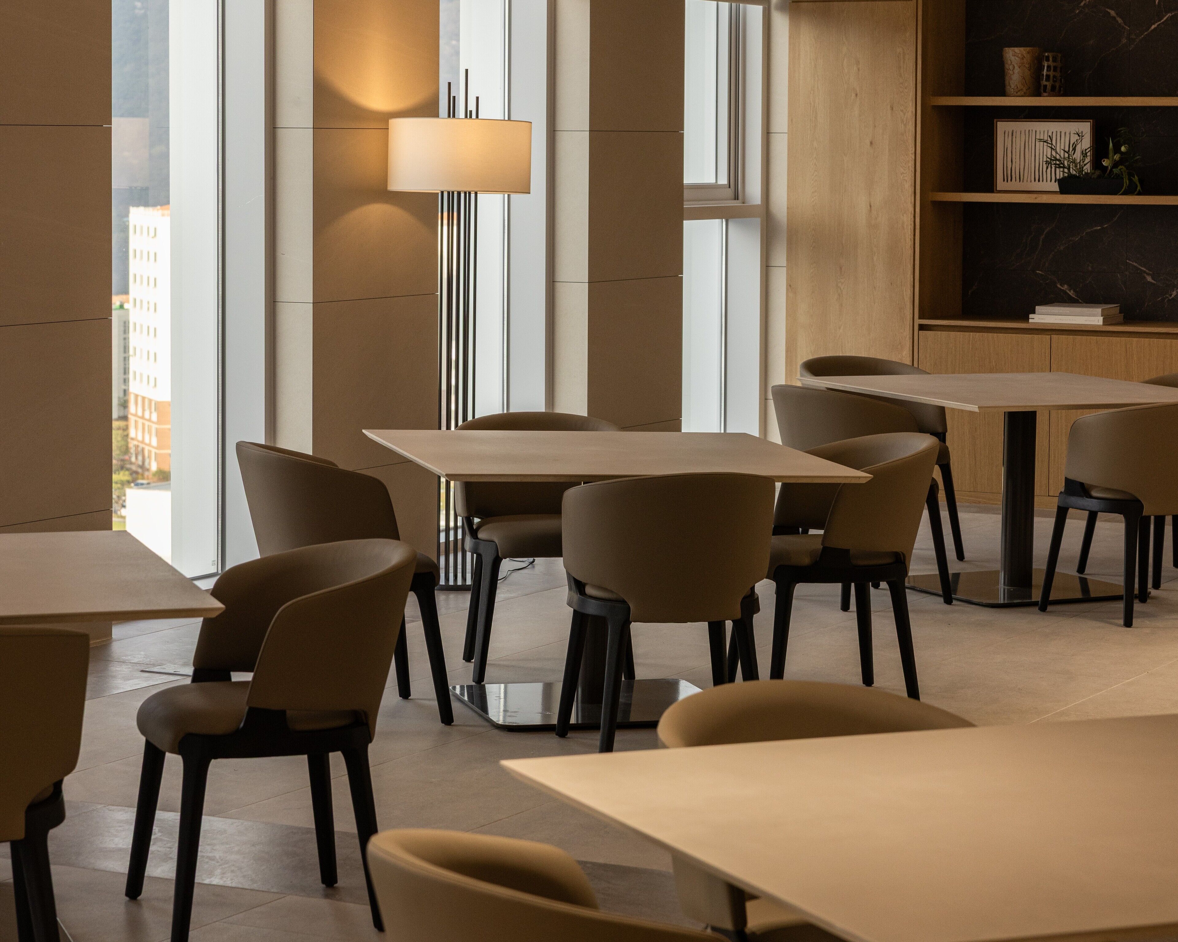 A modern dining area with multiple tables and chairs, large windows, and a minimalist decor.