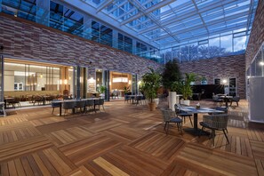 Un espacio interior amplio con suelo de madera, paredes de cristal y varios conjuntos de asientos.