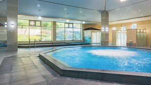 Una piscina interna con pareti in vetro trasparente, pavimento piastrellato e soffitto con illuminazione a incasso.