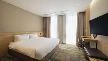 A hotel room with a large bed, a desk, a chair, and a TV.