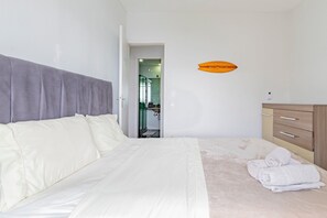 Un dormitorio con cama, cómoda de madera y baño visible a través de una puerta abierta.