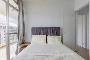 A bedroom with a bed, curtains, and a view of buildings through the window.
