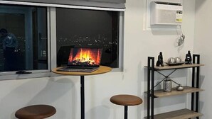 Een kamer met een laptop op een klein tafeltje, een plank met decoratieve objecten, en een raam met uitzicht op een stadsbeeld 's nachts.