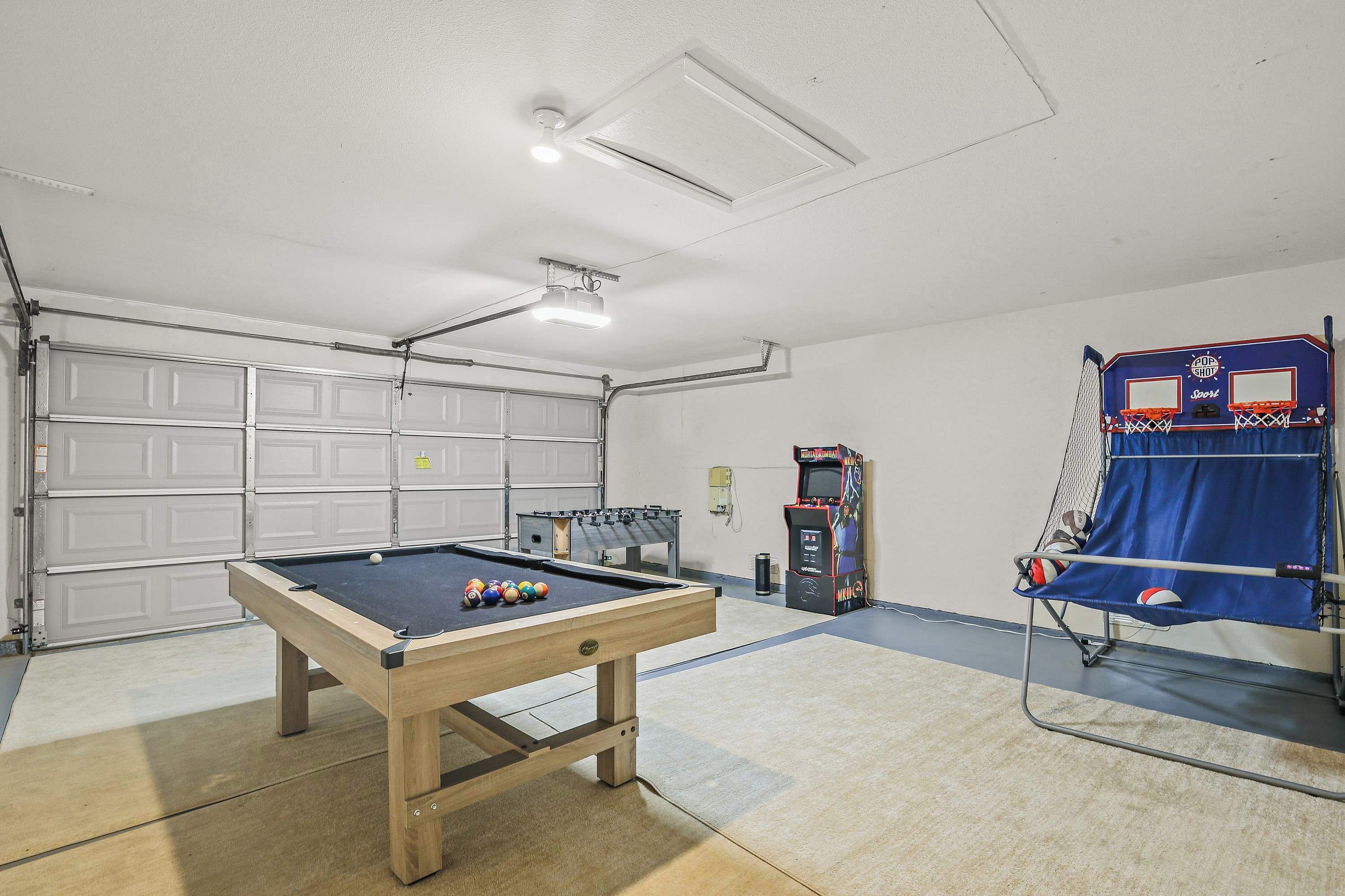 A pool table with balls, a ping pong table, and a basketball hoop in a garage.