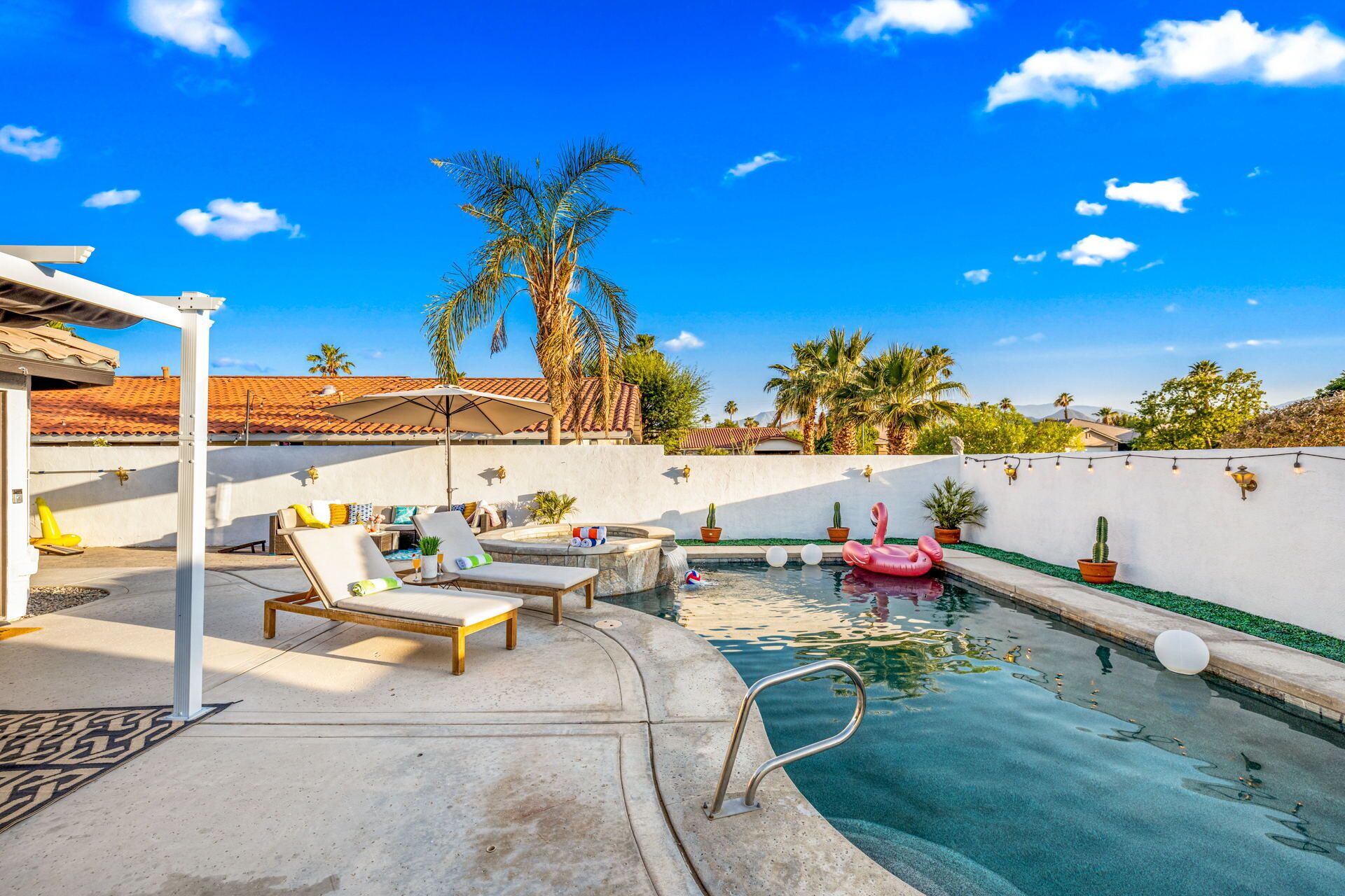 Un espace piscine aménagé avec des chaises longues, une petite piscine et des palmiers.
