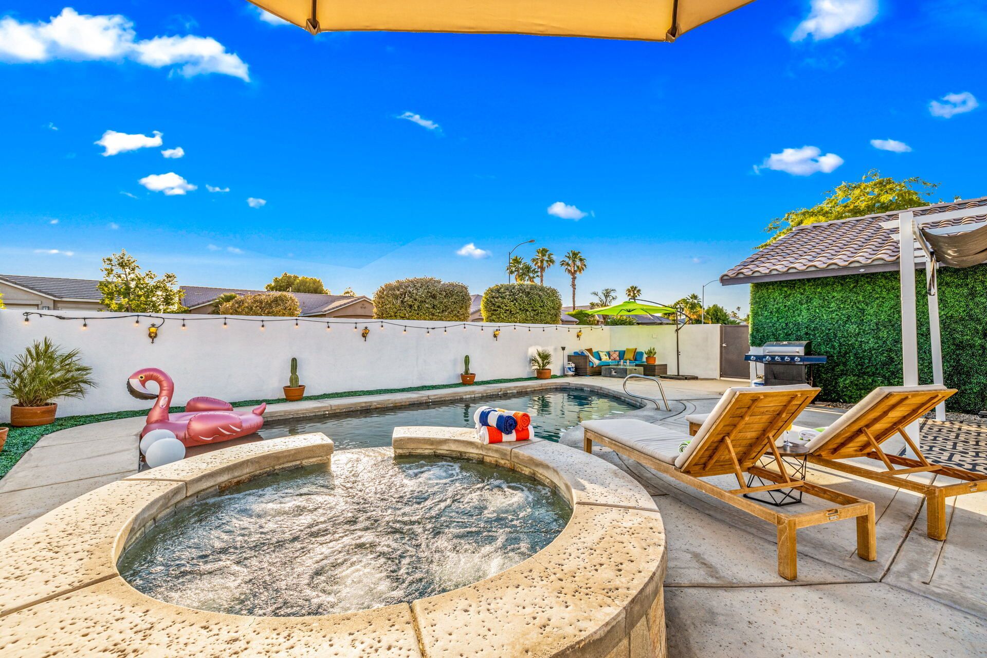 A backyard with a hot tub, lounge chairs, and a swimming pool.