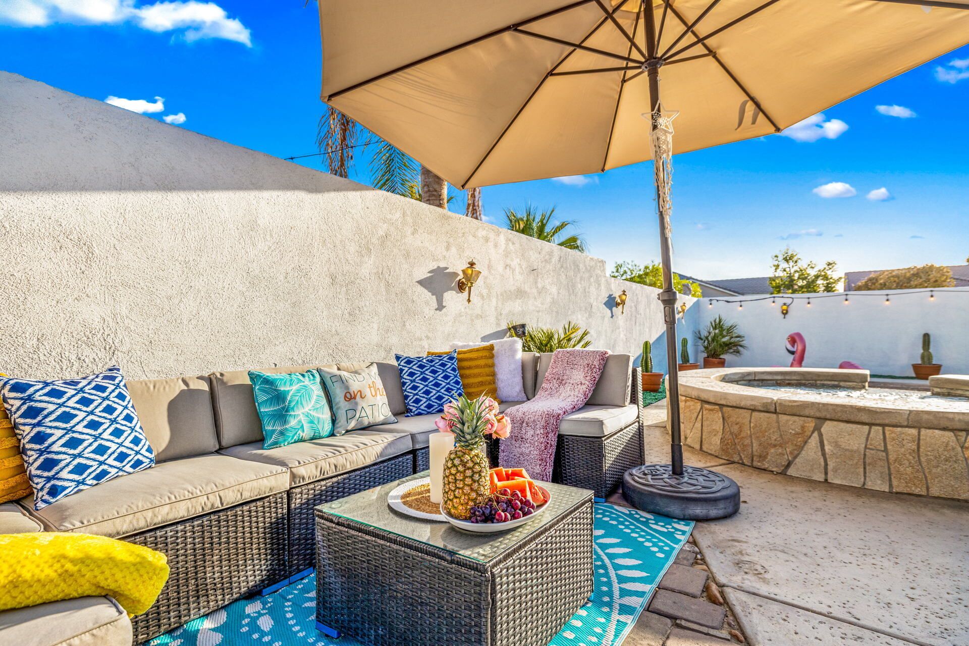 A patio with a sofa, cushions, a table with fruit, and a hot tub.