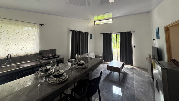 Una cocina moderna con zona de comedor, horno empotrado y un amplio ventanal con cortinas.