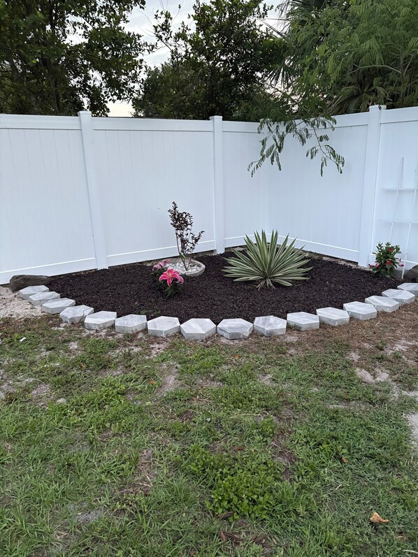 A landscaped garden area with a white fence, a variety of plants including a pink flowering plant, and a large agave plant. - Beachy Cocoa Home Near Cruise Port W/ Hot Tub (Cocoa)