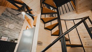Un escalier en colimaçon avec des marches en bois et des rampes en métal noir, dans une pièce aux murs en bois et ornée d’une horloge.