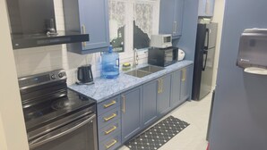 Una cocina moderna con armarios grises, una estufa negra, un dispensador de agua grande y un microondas.