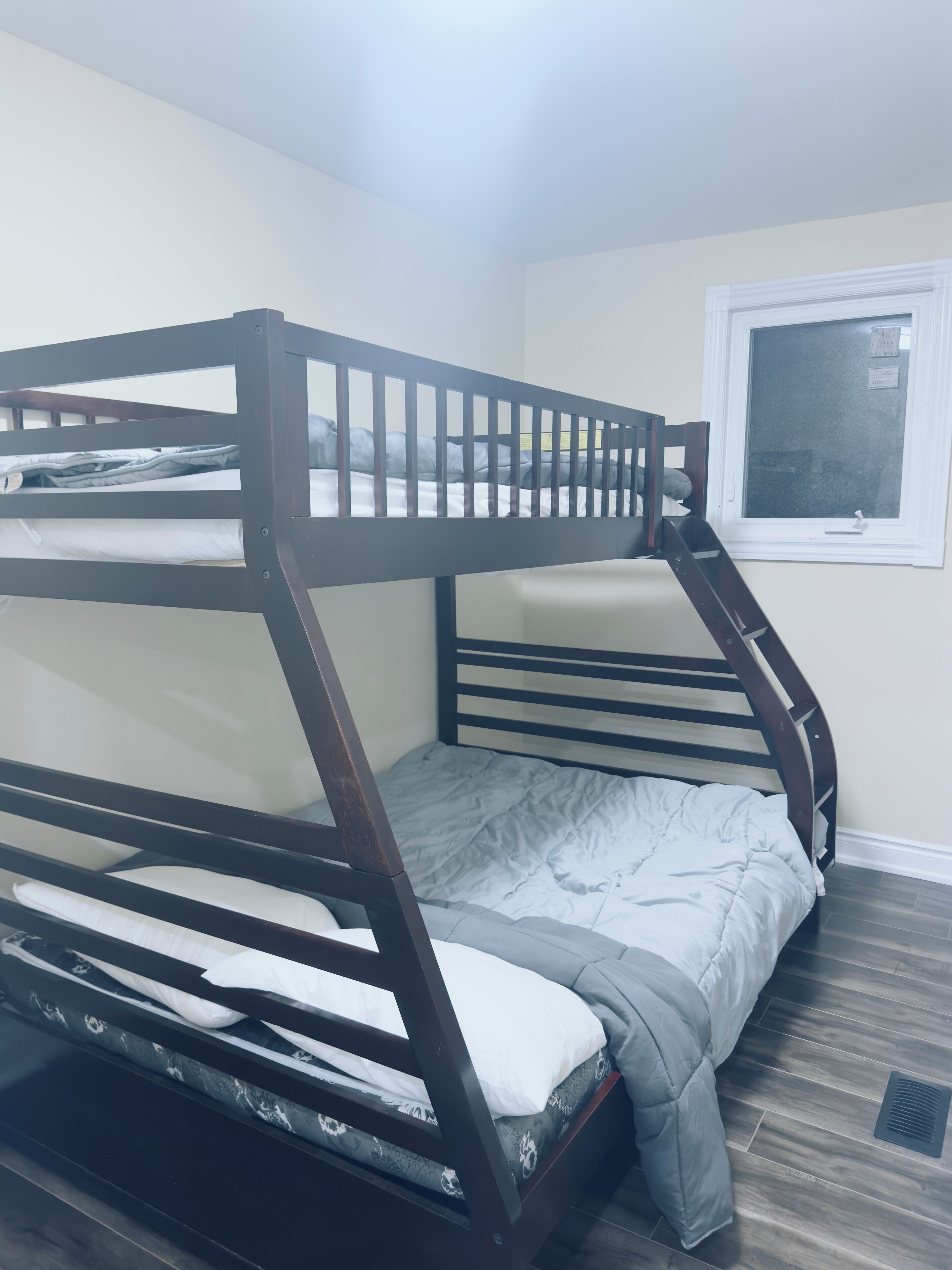 A bunk bed with a ladder, a window, and a vent on the floor.