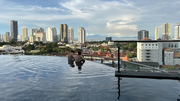 An infinity pool with a cityscape view, including high-rise buildings and a distant mountain range. - Food Paradise Georgetown 218 Macalister 2BR Family Suite By Smart Space Home (George Town)