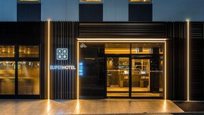 L’entrée d’un hôtel au design moderne, avec une façade en verre et une enseigne lumineuse.