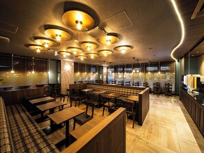 A modern restaurant interior with wooden furniture, a central bar area, and pendant lighting.