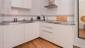 A modern kitchen with white cabinets, a stainless steel range hood, a microwave, and a wooden cutting board.