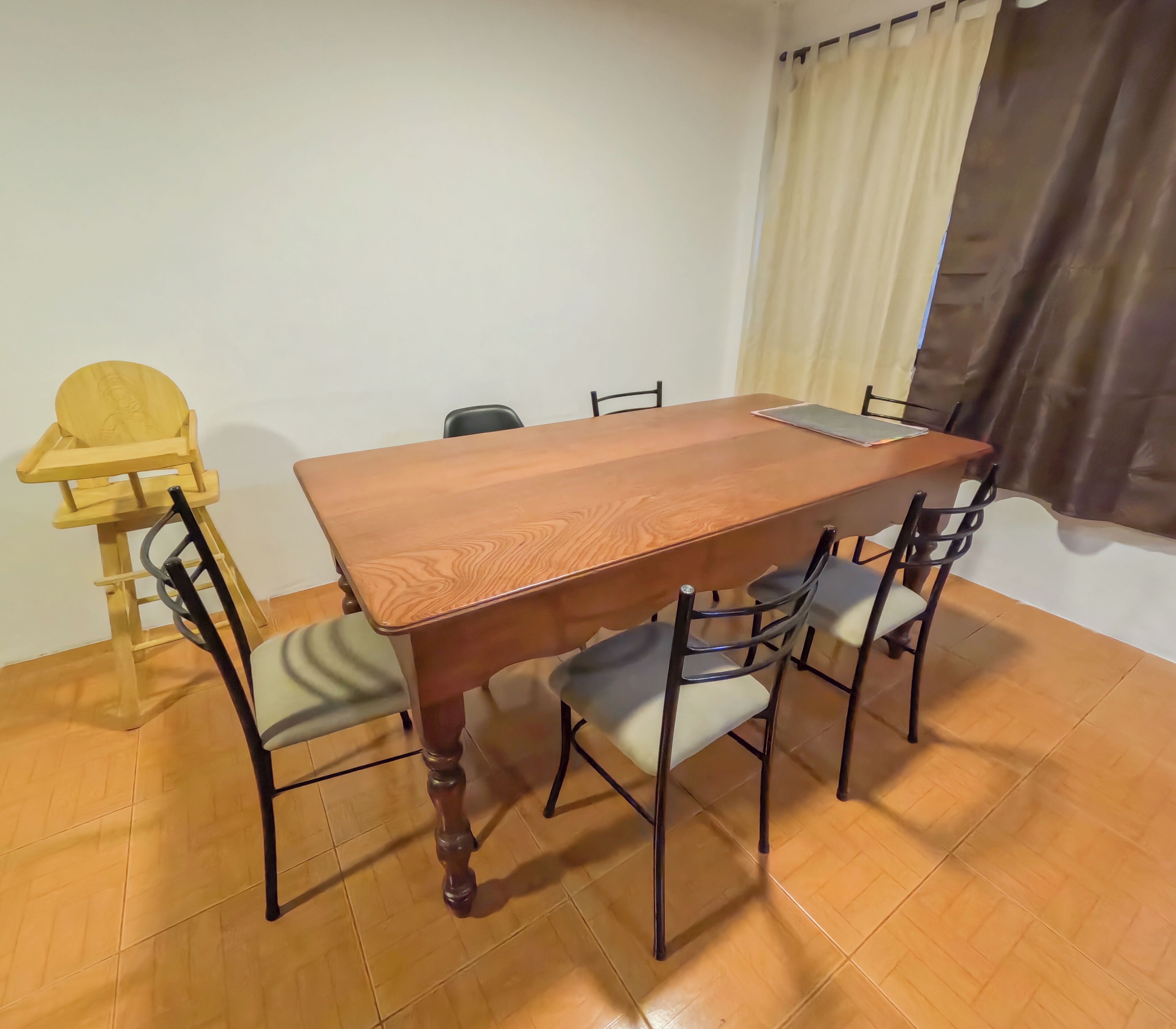 Uma área de refeições com uma mesa de madeira, quatro cadeiras e uma cadeira para bebê.