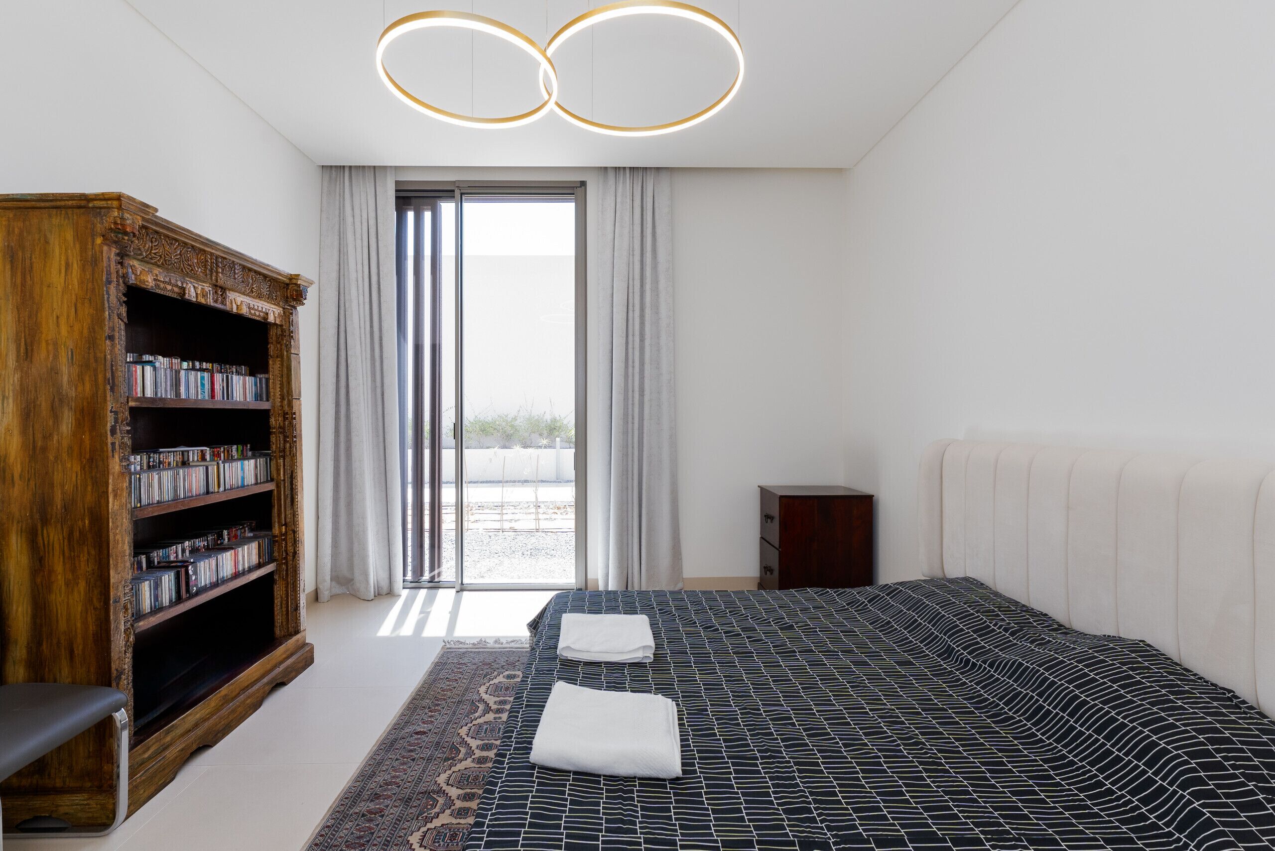 Ein modernes Hotelzimmer mit einem großen Bett, einer Holzbibliothek und Blick durch eine Glastür.