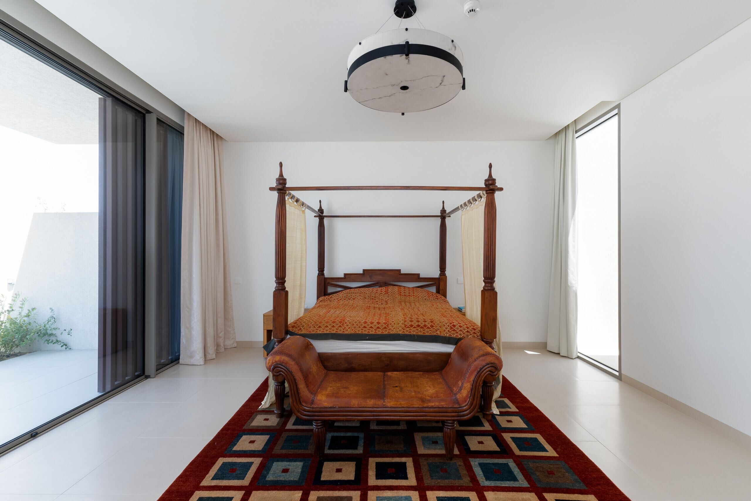 Une chambre à coucher avec un lit à baldaquin, de grandes fenêtres et un tapis à motifs.
