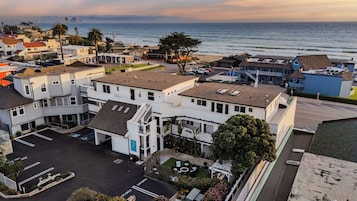 A coastal hotel with multiple buildings, a parking lot, and a view of the ocean.