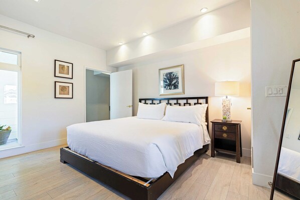 Un dormitorio moderno con una cama grande, una mesita de noche, un espejo y cuadros en la pared.