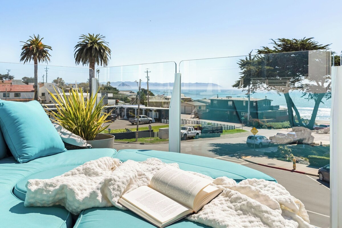 Ein Balkon mit einem blauen Sofa, einer weißen Decke und einem offenen Buch.