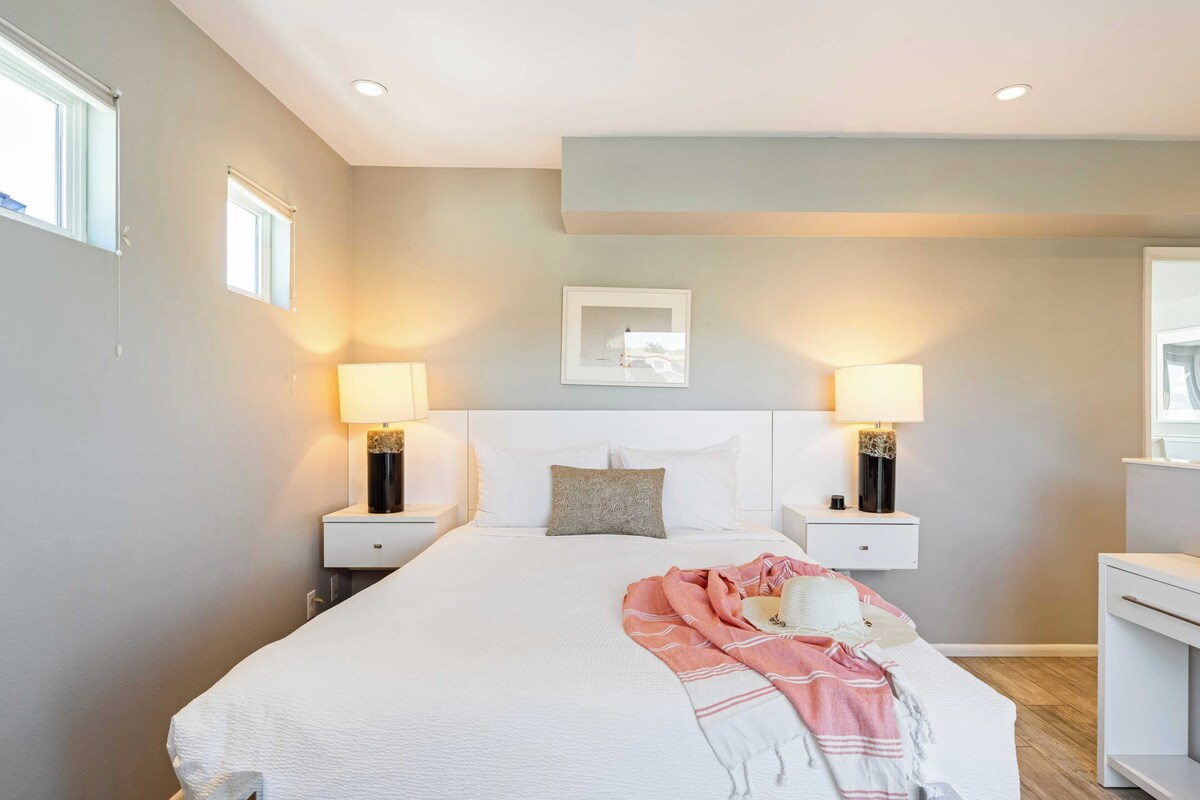 Een moderne slaapkamer met een groot bed, twee nachtkastjes met lampen, een hoofdbord en een ingelijste foto aan de muur.