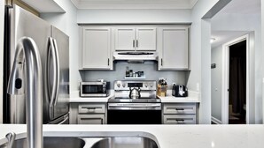 A modern kitchen with stainless steel appliances, white cabinetry, and a double sink. - Oceanfront Condo - Private Boardwalk - Pool & Balcony (St. Simons Island)