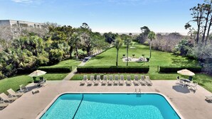 A swimming pool with a deck, surrounded by a well-maintained lawn, and a pathway leading to a building. - Oceanfront Condo - Private Boardwalk - Pool & Balcony (St. Simons Island)