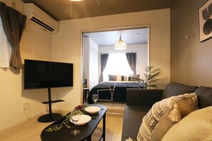 A modern living room with a flat-screen TV, a dining table with plates and wine glasses, a sofa, and a view into the bedroom with a bed and curtains. - Stellar Nishikoujiya 201  (Tokyo)