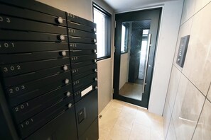 A hallway with a row of black mailboxes numbered 101 to 503, a door with a mesh screen, and a tiled floor. - Stellar Nishikoujiya 201  (Tokyo)