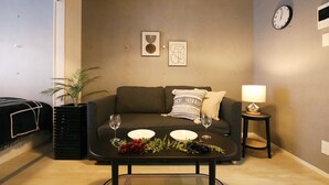 Een woonkamer met een bank, een salontafel met decoratieve objecten, een bijzettafeltje met een lamp, en een wandklok.