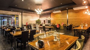 A restaurant with wooden tables and chairs, a brick wall, and hanging lights. - M Boutique Resort (Chiang Rai)
