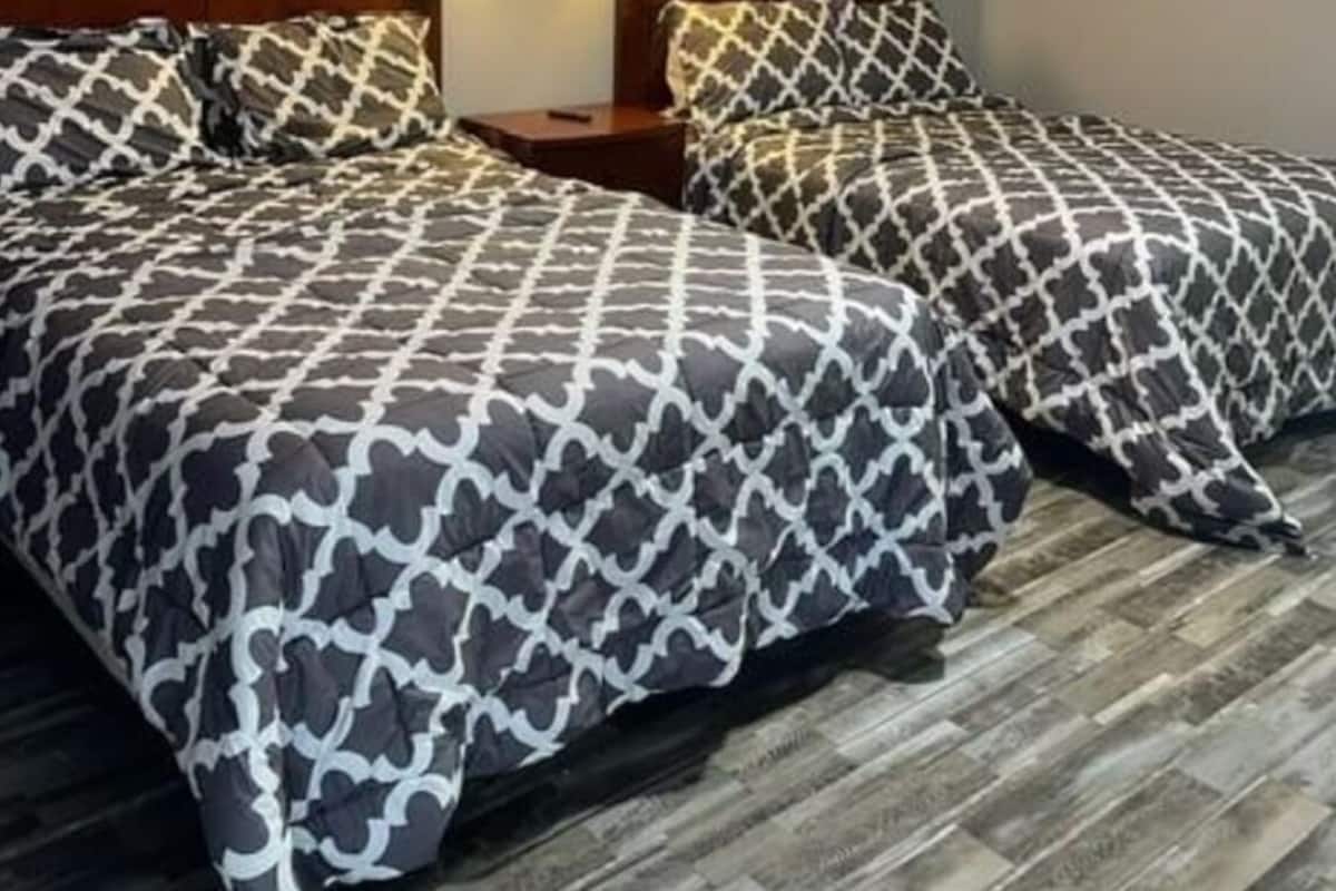 A hotel room with two beds, each with patterned bedding, wooden headboards, and bedside lamps.