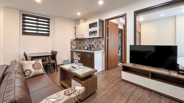 Una sala de estar moderna con sofá, una mesita de centro y televisor. Se observa una cocina con armarios y microondas.