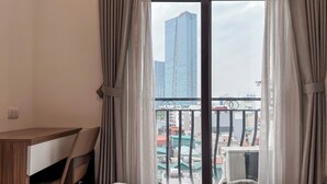 Habitación de hotel con cama, escritorio y silla. La habitación ofrece vistas a un paisaje urbano con edificios y un balcón.