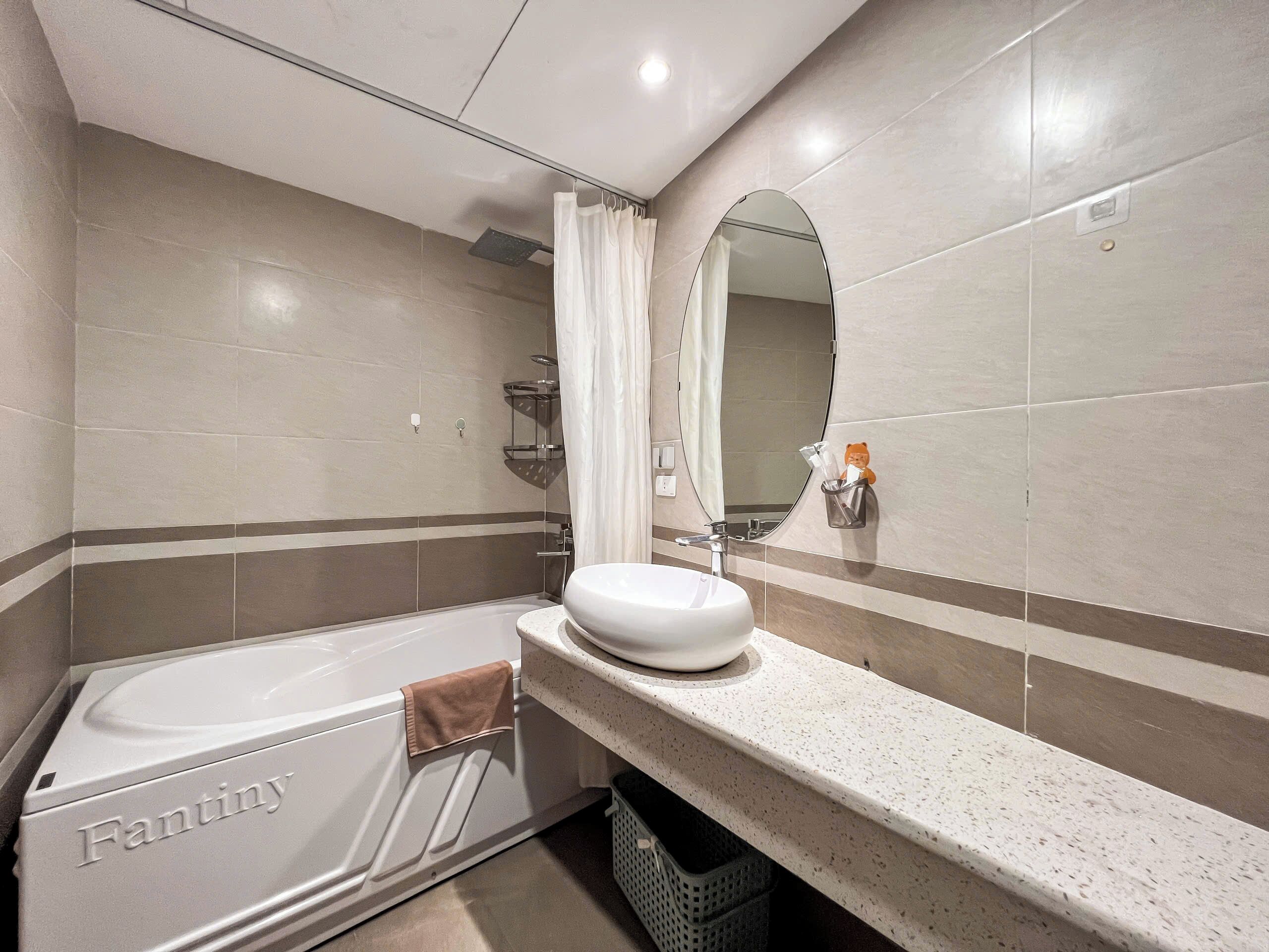 A modern bathroom with a white bathtub labeled 'Fantiny', a large mirror, and a sink with a towel rack.