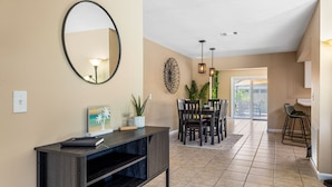 A modern interior with a dark console table, a round mirror, and a dining area with chairs and a table.