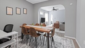 Un espace repas moderne avec une table et des chaises en bois, une console blanche et un téléviseur en arrière-plan.