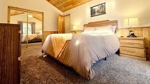 A bedroom with a wooden ceiling, a bed with a white comforter, a wooden nightstand, and a mirror on the wall.