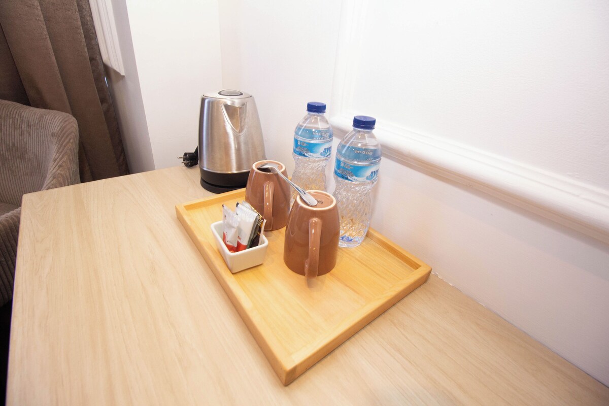 A wooden table with a tray containing a coffee pot, two mugs, and a small container with a spoon. Two water bottles are also on the table.