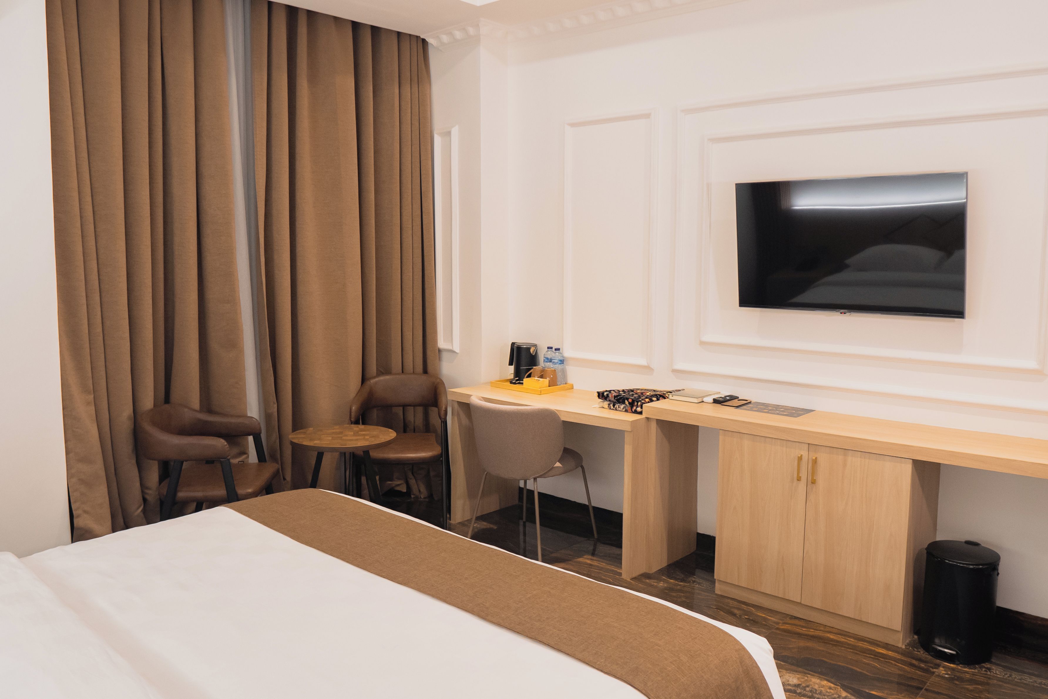 A hotel room with a bed, a desk, two chairs, a television, and a trash can.