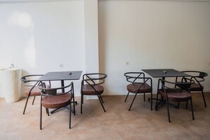 A dining area with four tables and chairs, a large pillar, and a tiled floor. - Fahira Hotel Syariah Padang (Padang)