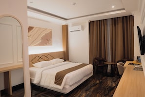 A hotel room with a bed, a desk, a chair, a TV, and an air conditioning unit. - Fahira Hotel Syariah Padang (Padang)