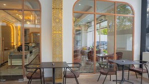 An interior with glass doors leading to a dining area, featuring tables and chairs. - Fahira Hotel Syariah Padang (Padang)