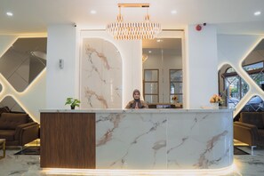 A reception desk with a marble top, a modern chandelier, and a potted plant. - Fahira Hotel Syariah Padang (Padang)